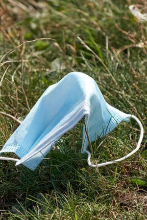 A used disposable blue face mask carelessly discarded on grass, during the Covid-19 pandemic.の写真素材