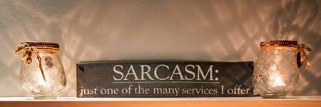 Glass candle holder with burning tea candle with reflection. Sign with text: sarcasm just one of the many services I offer. Banner, long cover or social media.の写真素材