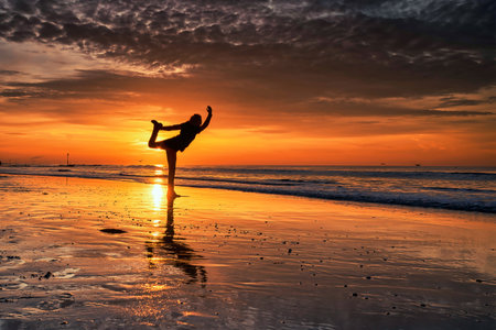 Silhouette of woman practicing yoga on the beach during a beautiful sunsetの写真素材
