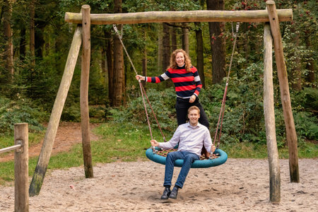 Young couple swings in the playground. the man and wife are in love. They look happy and laugh in...