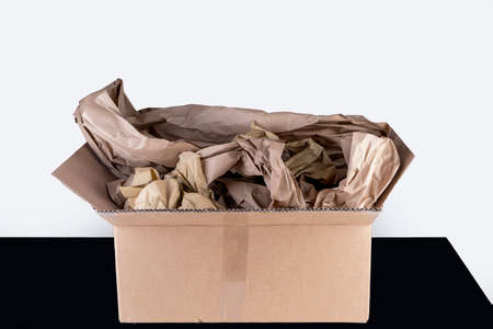 Open cardboard box on a black table, with paper filling. For safe transport during parcel service, reuse, environmentの写真素材