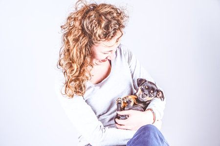 Part of a female, she lovingly holds a tiny sleeping Jack Russell Terrier puppy in her arms. Vintage, retro colorsの写真素材