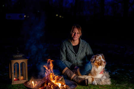 Dog sits by the campfire with his owner. The woman looks lovingly at the German Shepherd. Holiday in winter, candle fire in lanternの写真素材