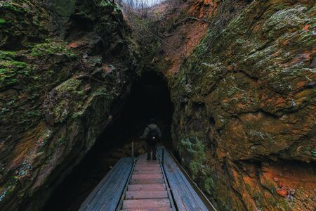Traveler with a backpack getting down into the cave by wooden stairs. Back view. In the mountainsの写真素材
