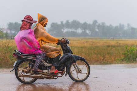 Kampot, Cambodia - December 14, 2016: two persons in packable raincoats ride a motorbike while heavy raining.のeditorial素材