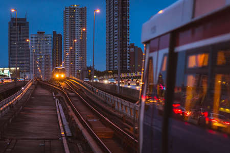 Bangkok, Thailand - June 25, 2019: a BTS train arrives in Saphan Taksin station at night. High-rise buildings of Khlong Ton Sai, Khlong San in the background.のeditorial素材