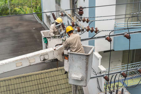 Electricians in the uniform are fixing a power line, being on aerial work platforms of a repair truck. A concept of power outage / blackout.の写真素材