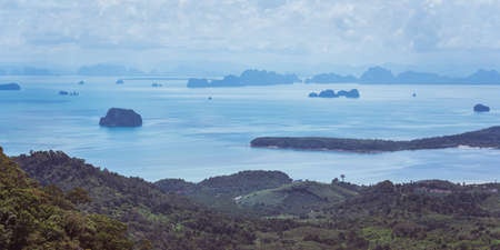Beautiful tropical panorama of hilly coastline and smooth sea space with numerous rocky islands and islets under the curly sky. Traveling in Krabi Province, Thailand.の写真素材