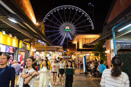 Bangkok, Thailand - July 28, 2019: a crowded alley at Asiatique The Riverfront at night, with a view of the Ferris wheel. The Asiatique is a popular touristy shopping and entertainment space.のeditorial素材