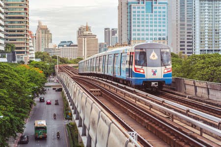 Bangkok - June 25, 2019: a BTS train travels towards Ratchadamri station with the outlines of the downtown (Bang Rak District, Si Lom) in the background.のeditorial素材