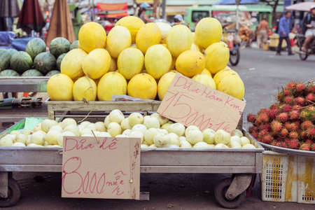 Melons on stalls with price tags: golden melon, 15.000 dongs (0.6 USD) for 1 kg, and pear melon, 8.000 dongs for a piece. At a street market in Cho Lon, Ho Chi Minh City, Vietnam.の写真素材