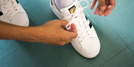 Bangkok, Thailand - May 20, 2019: a man laces white Adidas Superstar sneakers.