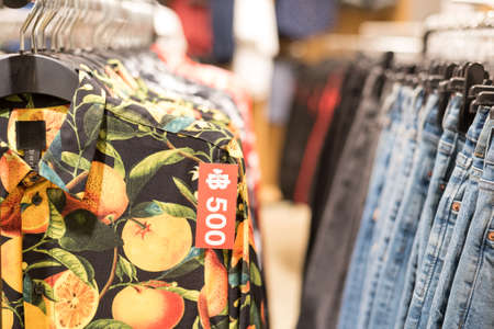 Bangkok, Thailand - May 19, 2019: a close up of a H&M shirt with orange tree pattern and a price tag 500 baht on it and rows of clothes hanging in a H&M store at Mega Bangna shopping mall.のeditorial素材