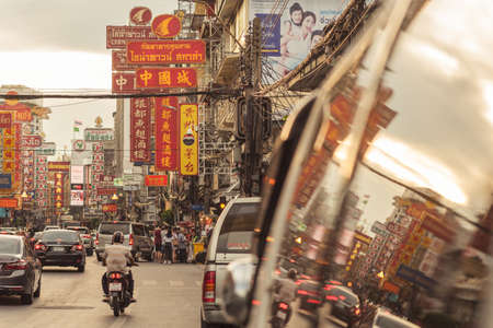 Bangkok, Thailand - June 2, 2019: the main artery of Chinatown, Yaowarat Road in the evening, with its large signboards written in Chinese and reflection in the window of a parked car.のeditorial素材
