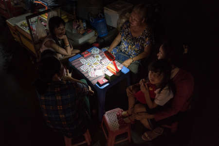 Phnom Penh, Cambodia - February 6, 2019: women and girls listen to an elderly fortune teller, sitting in front of a table with playing cards in the night street.のeditorial素材