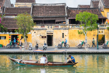 Hoi An, Vietnam - October 28, 2018: the old town riverside street with travelers in a boat and cycle rickshaws.のeditorial素材