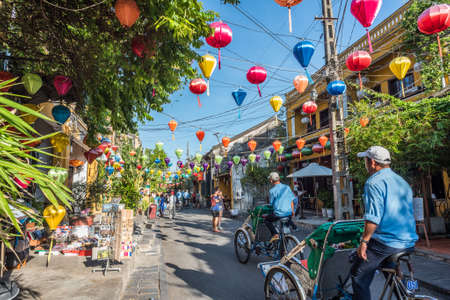 Hoi An, Vietnam - October 24, 2018: two rickshaws drive along a colorful street of the old town decorated by lanterns.のeditorial素材