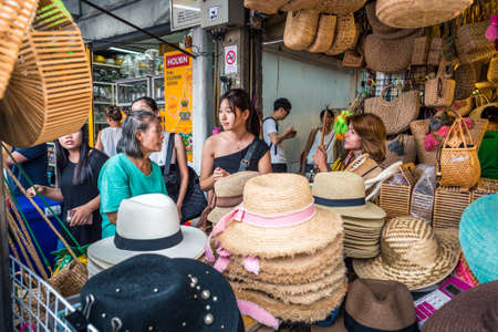 Bangkok, Thailand - May 13, 2018: three women talk to each other behind a shop counter filled with hats and wicker bags at Chatuchak Weekend Market.のeditorial素材