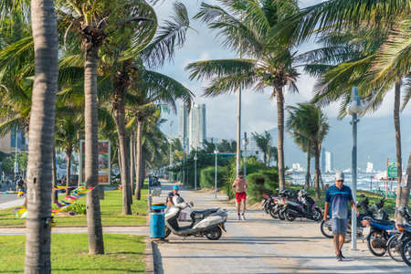 November 8, 2018 - Da Nang, Vietnam: the sidewalk of the seaside street (Vo Nguyen Giap) along My Khe beach with palm trees sway in wind, people sit, walk, jog and sea waves visible in the background.のeditorial素材