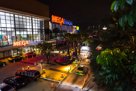 Bangkok, Thailand - August 17, 2018: Mega Bangna Shopping Mall exterior at night with a street (parked cars, taxis, trees, people walk) in front of it.のeditorial素材