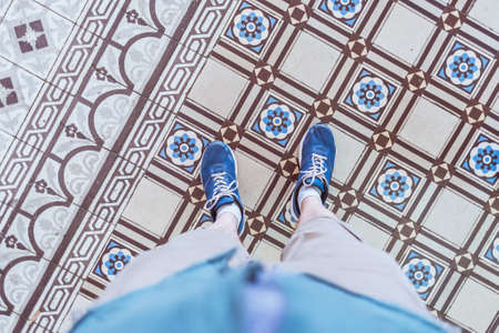Old tiles of historical building of Saigon Central Post Office (Ho Chi Minh City, Vietnam) constructed in 1886-1891. Beautiful detail of interior, a selfie of blue sneakers on antique tiled floor.の写真素材