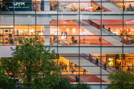Bangkok, Thailand - June 15, 2018: life of EmQuartier Shopping Mall through the glass at night. In the foreground, trees in the dusk of a courtyard garden of the shopping center.のeditorial素材