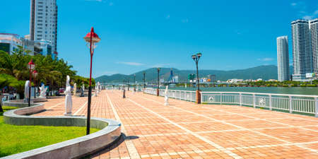 Da Nang, Vietnam - May 7, 2018: The Han River embankment - Bach Dang Street. The empty cobblestone sidewalk with street lights, the handrail, trees and view of the city, river and distant mountains.のeditorial素材