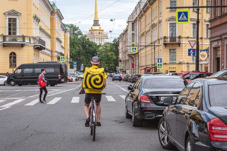 Saint Petersburg, Russia - July 30, 2021: a food delivery man of Yandex.Eda on a bike rides down Voznesensky Avenue.のeditorial素材