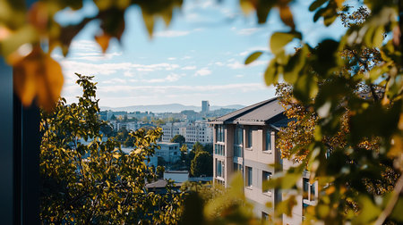 A scenic view of a city skyline with modern buildings, framed by vibrant autumn leaves. The composition captures the blend of urban and natural elements under a bright sky.の素材