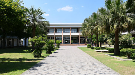 A modern building with large windows is framed by palm trees and lush greenery, leading to a patterned stone walkway under a clear blue sky.の素材