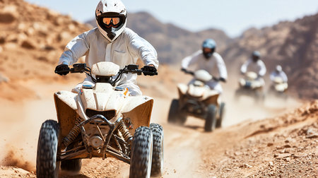 A beige ATV, covered in dirt, is being driven by a person wearing white clothing and a helmet with goggles. The ATV has black tires.の素材