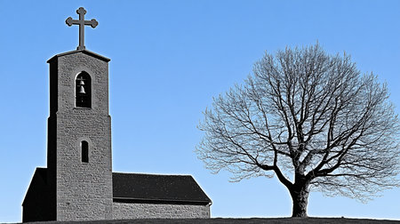 Stone church featuring a cross atop its bell tower, which houses a bell, positioned next to a large, leafless tree with intricate branches.の素材