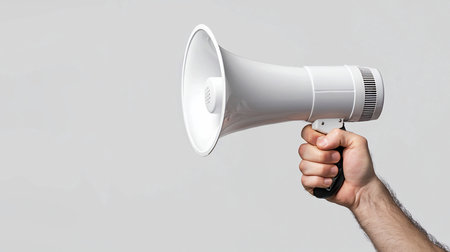 A white megaphone held in a hand, with a black handle, ready to be used. The megaphone is clean and new.の素材