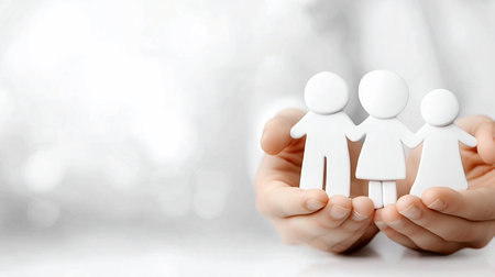Cupped hands securely hold three smooth, white, minimalist family figures, a man, woman, and child, standing united.の素材