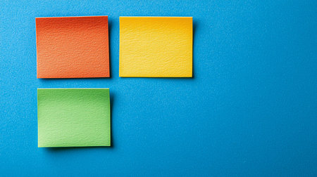 Three square, blank sticky notes in vibrant orange, yellow, and green. The paper has a noticeable, slightly rough texture and clean-cut, straight edges.の素材