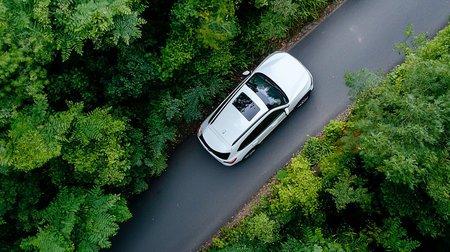 A white modern SUV in motion, featuring a reflective body, a large black glass sunroof, and sleek aerodynamic lines. The vehicle has black window trim and roof rails.の素材