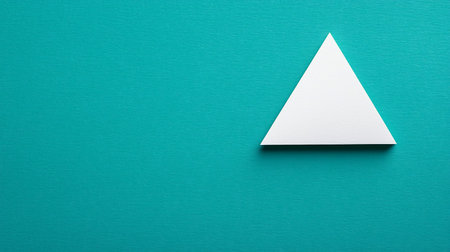 A crisp white paper triangle with a subtle texture, resting on a textured teal surface, creating a clean, minimalist aesthetic.の素材