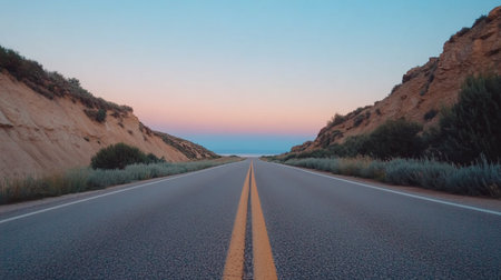 An empty asphalt road with double yellow lines extends into the distance, flanked by hills under a colorful sunset sky, suggesting a journey or escape.の素材