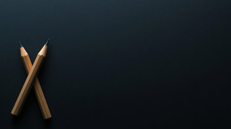 A close-up view of two simple wooden pencils, sharpened and crossed over each other, resting on a plain, dark surface, suggesting readiness for creative or academic tasks.の素材