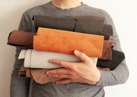 the tanner holds leather in his hands in rolls of different colors.