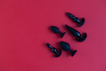 Black silicone sex toys on a red background. Erotic toy for fun. Diffrent anal butt plugs. View from above with space for textの写真素材