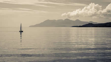 Distant sailboat on calm waters with mountains in the distance   Black and whiteの写真素材