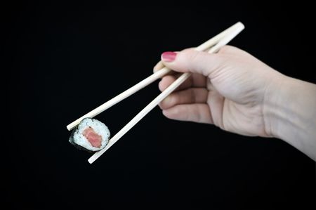 Asian Raw Fish Sushi Food in Chopsticks isolated on solid black .  Healthy dinner being held by the hand of a female model.の写真素材