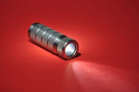 Small Custom Pocket Flashlight Shining On Red Background Gradientの写真素材