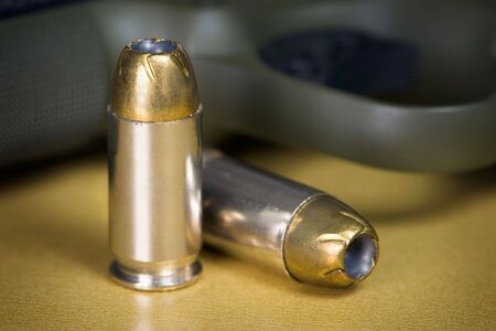 .45 Caliber Hollow Point Pistol Bullets Standing Near Handgun on gold colored backgroundの写真素材