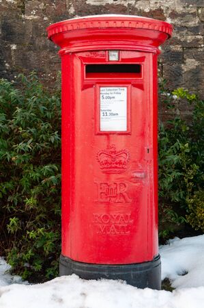 A traditional red British Post Box in a snowy rural setting. An old fashioned pillar box with snow on the ground.の写真素材