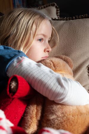 Pretty young blonde girl cuddling her teddy with her head on a cushionの写真素材
