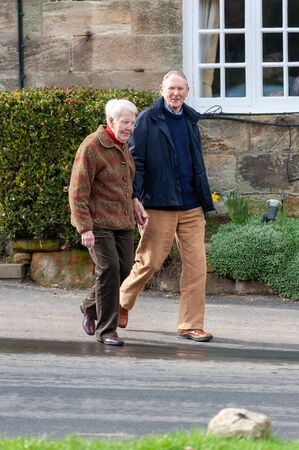 Elderly couple holding hands as they cross a road in a rural settingの写真素材
