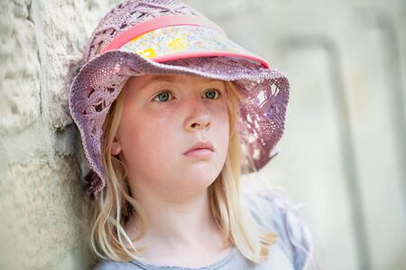 Melancholy pretty young blonde girl in purple hat. Blurry background with copy spaceの写真素材