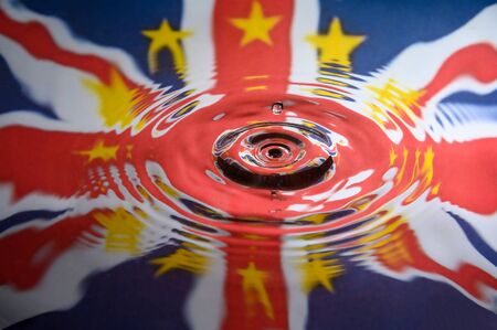 UK Union Jack and the stars of the European Union reflected in a water splash with a single drop of water falling. Abstract Brexit background.の写真素材